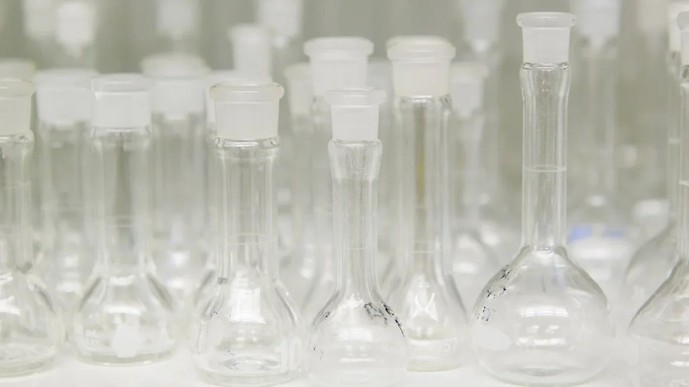 Several empty glass laboratory flasks with wide bases and narrow necks are arranged closely together, all sealed with glass stoppers.